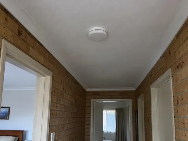 Ceiling smoke alarm in a brick hallway with white trim in Shortland